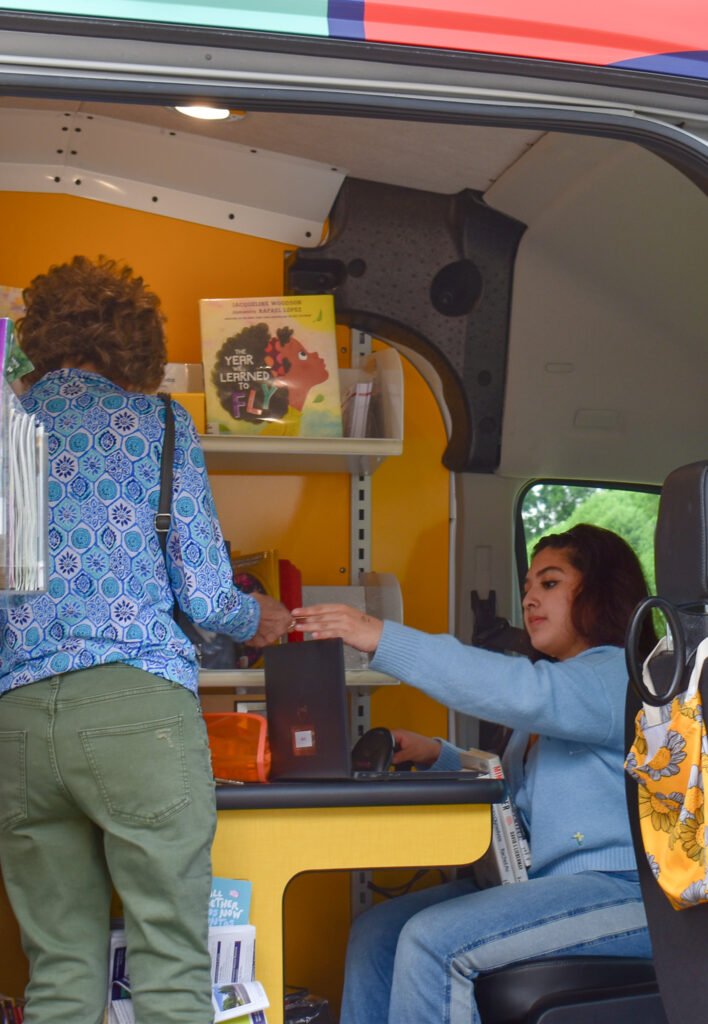 young woman handing a library card to a person inside a van