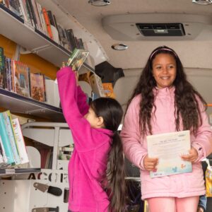 young girl holding a book smiling inside a bookmobile