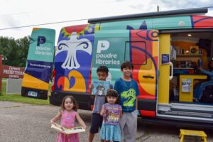 4 siblings smiling outside a colorful library bookmobile