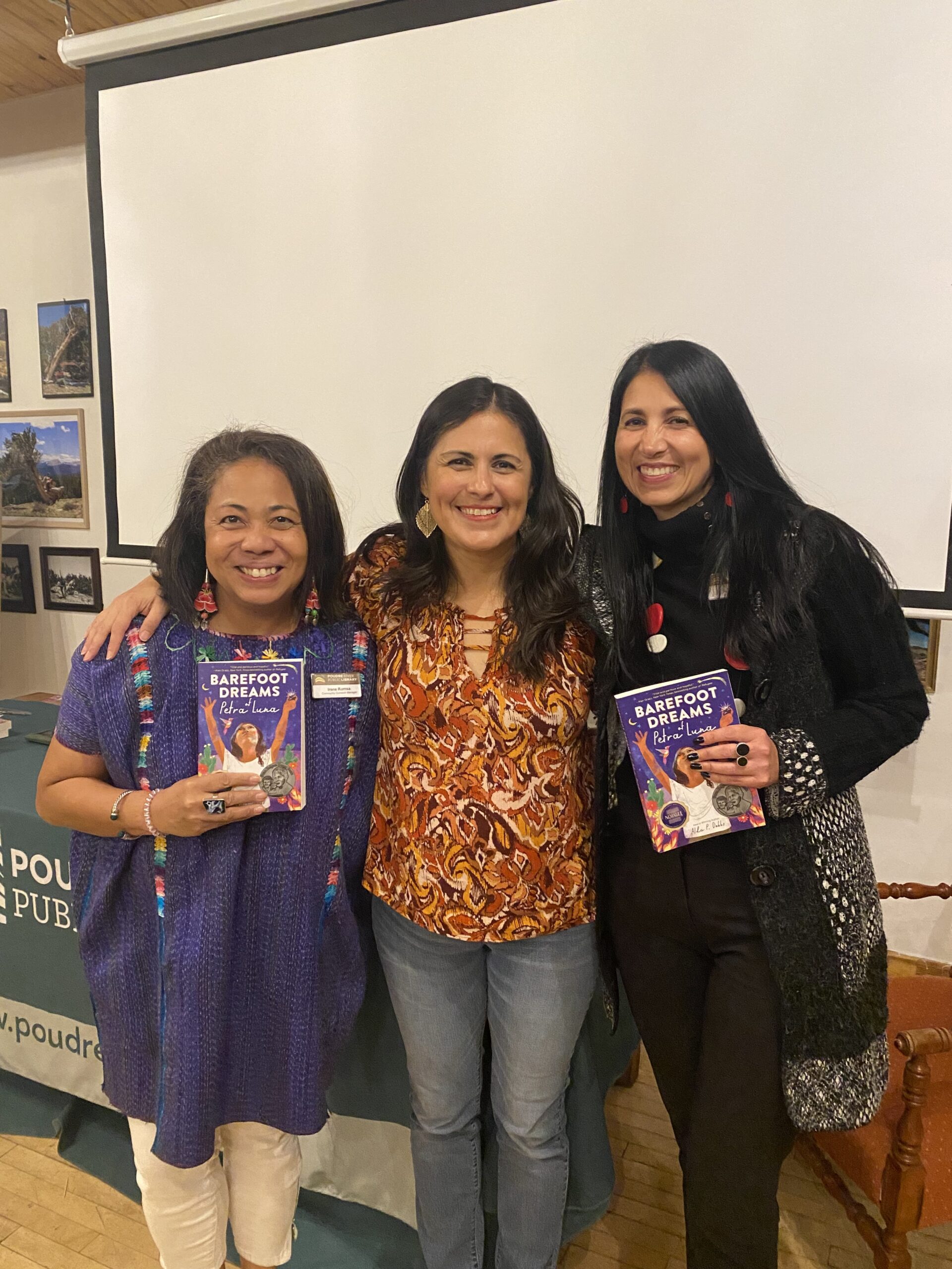 three Latina women smiling, two of them holding books